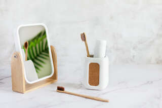 bamboo toothbrushes in a cup toothpaste and mirror on white marble table in a bathroom