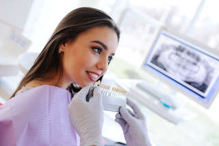 the dentist selects a young pretty girl for the patient a shade of teeth and shows on the monitor